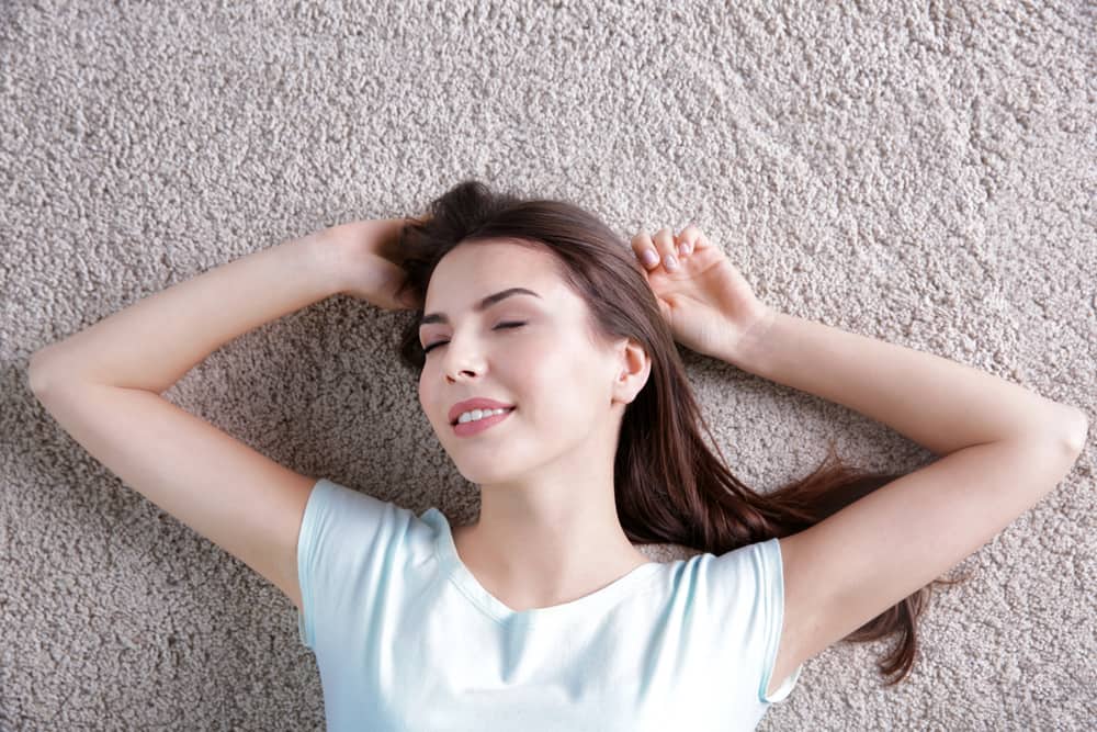 Happy young woman lying on carpet flooring